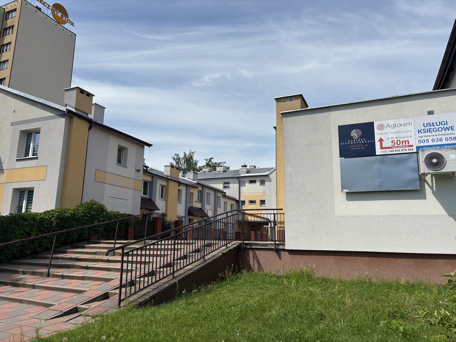 Dojście do gabinetu — chodnik i schody prowadzące do budynku z banerem „Gabinet Psychoterapii, ul. Witosa 25 lok. 33” oraz strzałką wskazującą wejście